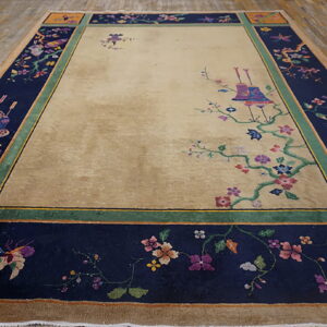Beige field rug with a wide navy border featuring colorful floral and butterfly designs on wood floor.