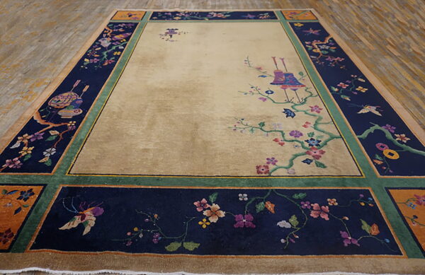 Beige field rug with a wide navy border featuring colorful floral and butterfly designs on wood floor.