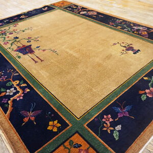 Camel rug with a dark navy border patterned with colorful flowering vines, birds, and butterflies on wood floor.