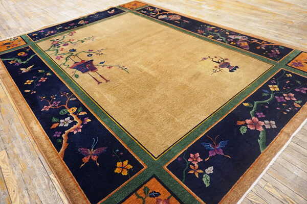 Camel rug with a dark navy border patterned with colorful flowering vines, birds, and butterflies on wood floor.