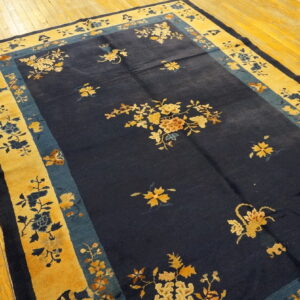 Navy area rug with gold and teal floral borders featuring scattered blossoms on light hardwood flooring.