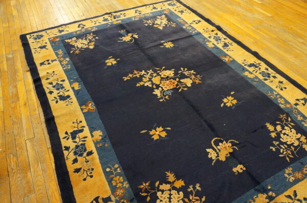 Navy area rug with gold and teal floral borders featuring scattered blossoms on light hardwood flooring.