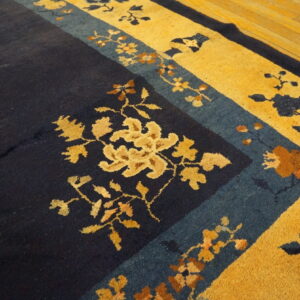 High-pile rug with navy blue field and golden yellow floral border resting on wood planks.