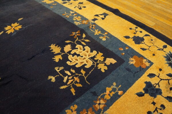 High-pile rug with navy blue field and golden yellow floral border resting on wood planks.