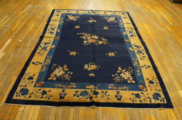Rectangular blue and gold rug with ornate floral patterns displayed on distressed hardwood floors.
