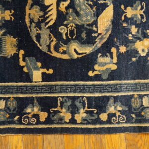 Navy blue rug with gold and light blue stylized pattern motifs and a key border sits on hardwood floors.