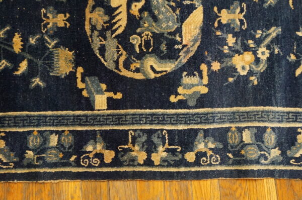 Navy blue rug with gold and light blue stylized pattern motifs and a key border sits on hardwood floors.