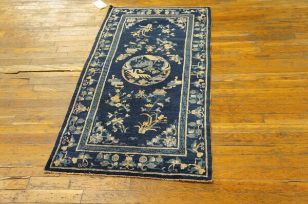 Dark blue rug featuring pale yellow floral motifs and a central medallion on distressed wood floors.