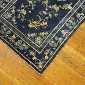 Dark blue rug with gold and light blue floral patterns lies on worn wood plank flooring.