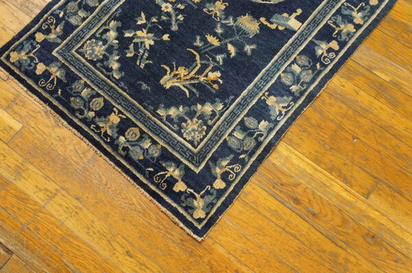Dark blue rug with gold and light blue floral patterns lies on worn wood plank flooring.
