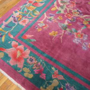 Close-up of a magenta and teal rug featuring a multicolored floral and vine pattern on hardwood floor.