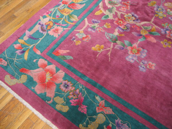 Close-up of a magenta and teal rug featuring a multicolored floral and vine pattern on hardwood floor.