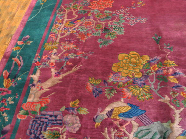 Magenta rug with teal border showcases a multicolored scenic pattern including flowers and a blue bird on wood floor.