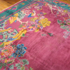 Magenta rug with colorful floral and bird patterns and a teal border lies on glossy hardwood floors.