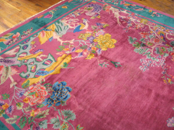 Magenta rug with colorful floral and bird patterns and a teal border lies on glossy hardwood floors.