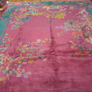 Deep pink rug with a wide teal border featuring multi-colored floral and bird motifs on wood flooring.