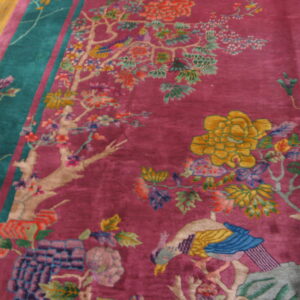 Ornate magenta rug featuring colorful tree, flower, and bird motifs on wood floor.
