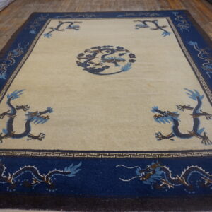 Beige field rug with a dark blue dragon medallion and border displayed on distressed wood flooring.