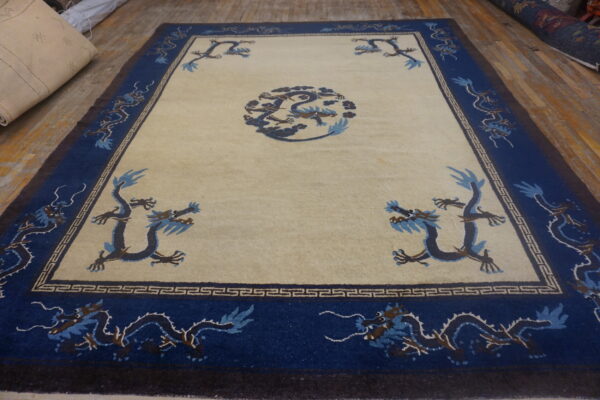 Beige field rug with a dark blue dragon medallion and border displayed on distressed wood flooring.