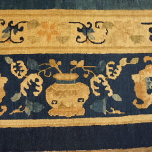 The rug border features ornate tan and blue floral motifs, including a central vase design.