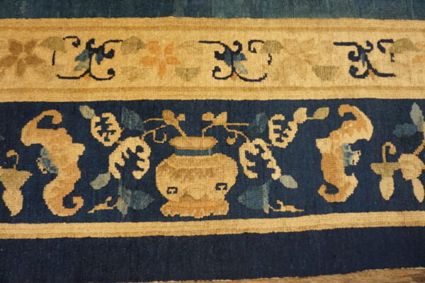 The rug border features ornate tan and blue floral motifs, including a central vase design.