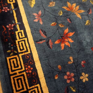 Dark blue high pile rug with autumn floral vines and a golden Greek key border on wood flooring.