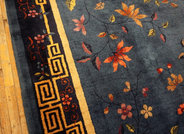 Dark blue high pile rug with autumn floral vines and a golden greek key border on wood flooring.