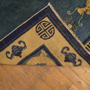 Blue rug with yellow-gold dragon and medallion patterns, folded back over a rustic wood floor.
