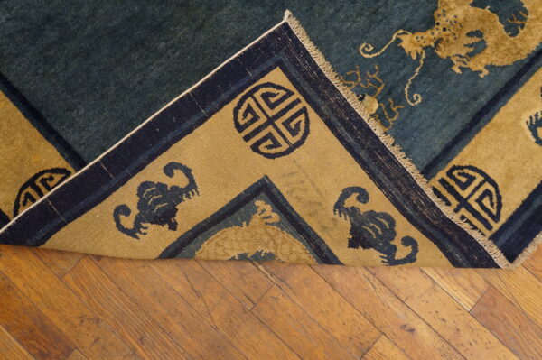 Blue rug with yellow-gold dragon and medallion patterns, folded back over a rustic wood floor.