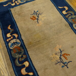 A low-pile tan rug featuring a decorative dark blue border rests on bright wood planks.