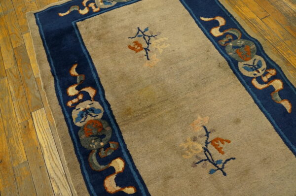 A low-pile tan rug featuring a decorative dark blue border rests on bright wood planks.