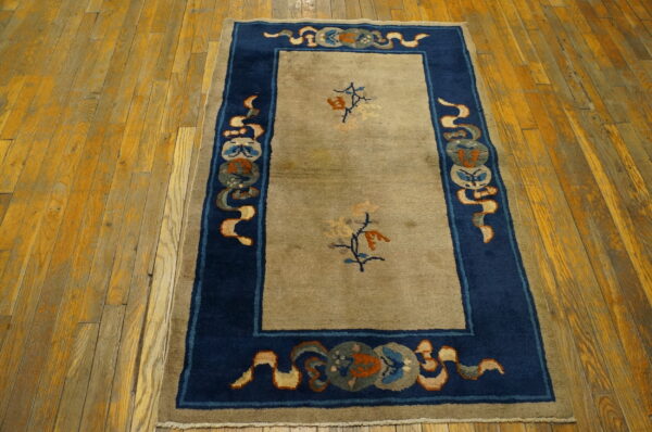 Tan area rug with a wide blue border, antique-style medallions, and low pile on distressed wooden planks.