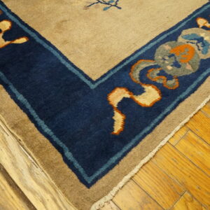 High pile rug corner featuring a beige field and dark blue border with orange and gray details on a wood floor.