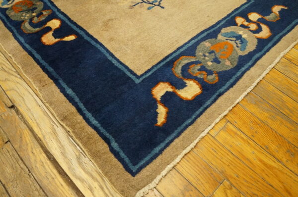 High pile rug corner featuring a beige field and dark blue border with orange and gray details on a wood floor.