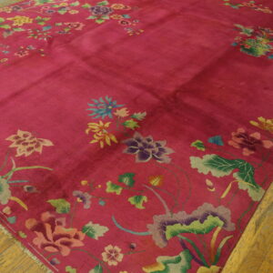 Bright pink rug featuring scattered large floral and leaf designs lies on distressed hardwood floor.