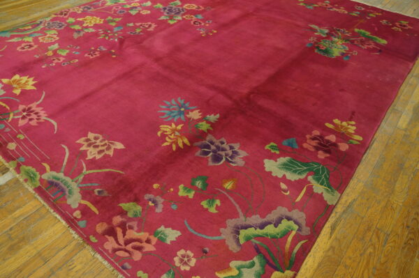 Bright pink rug featuring scattered large floral and leaf designs lies on distressed hardwood floor.