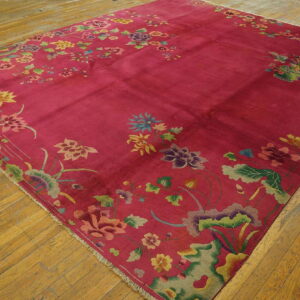 A magenta rug featuring a detailed multicolored floral border is placed on distressed hardwood flooring.