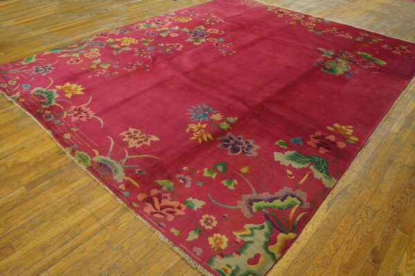 A magenta rug featuring a detailed multicolored floral border is placed on distressed hardwood flooring.