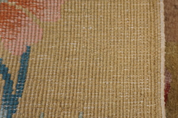Close-up of a textured tan rug with tight vertical ridges and small woven accents of pink and teal blue.