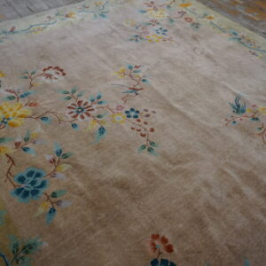 A low-pile tan rug with a colorful floral and vine pattern lies on distressed wooden floors.