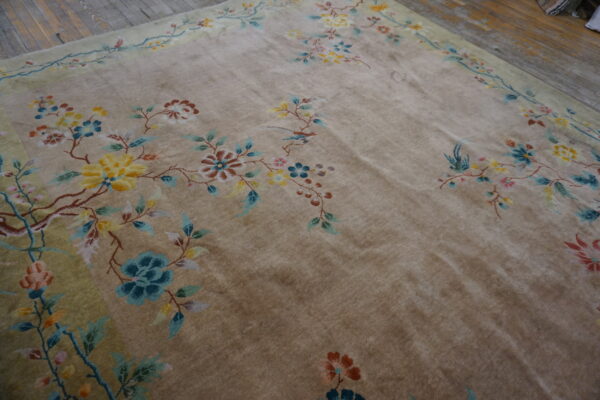 A low-pile tan rug with a colorful floral and vine pattern lies on distressed wooden floors.