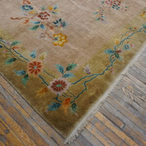 Light gold rug with a detailed multicolored floral border rests on distressed gray and tan wood flooring.