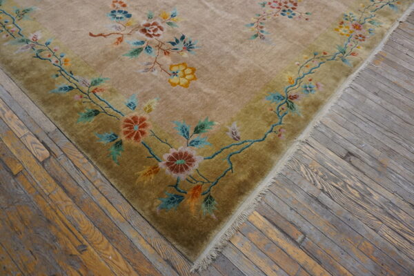 Light gold rug with a detailed multicolored floral border rests on distressed gray and tan wood flooring.