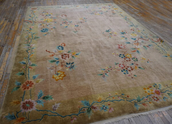 Taupe plush rug with colorful floral sprays and olive border lying on weathered wood flooring.