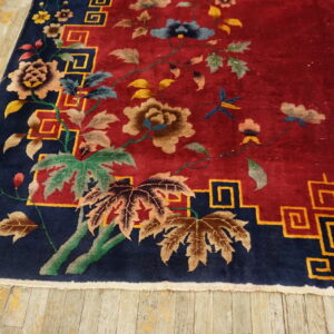 Red rug with a floral pattern and navy blue border with yellow key motifs on distressed wood flooring.