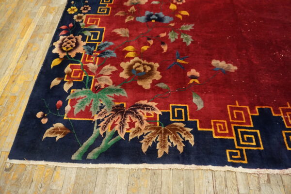Red rug with a floral pattern and navy blue border with yellow key motifs on distressed wood flooring.