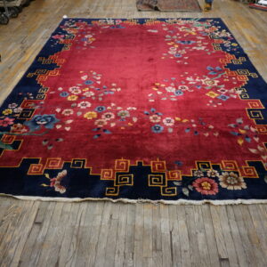 Red rug with scattered flowers and a navy key-pattern border rests on worn wood flooring.