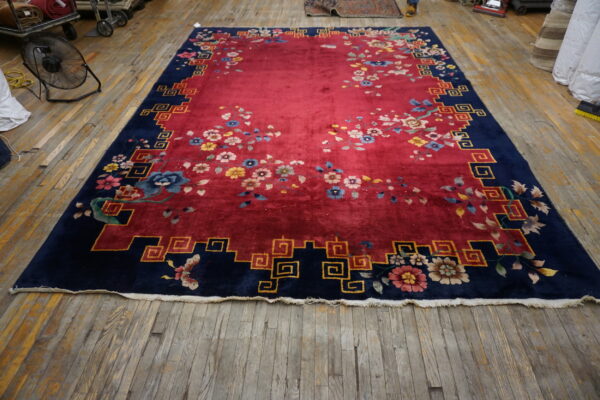 Red rug with scattered flowers and a navy key-pattern border rests on worn wood flooring.
