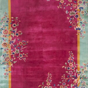 Magenta rug with a seafoam green border framed by gold, featuring detailed multicolored floral patterns.