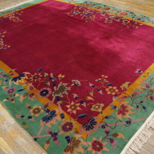 Lustrous magenta rug with a wide floral green border and gold trim rests on worn wooden flooring.